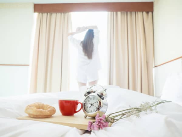 朝日を浴びて背伸びする女性とベッドの上の朝食